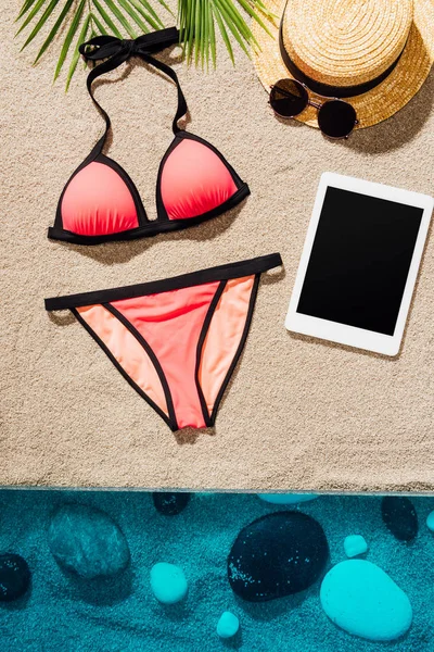 Top view of stylish pink bikini with accessories and tablet on sandy beach — Stock Photo