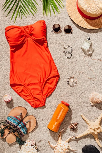 Top view of stylish red swimsuit with various accessories on sandy beach — Stock Photo