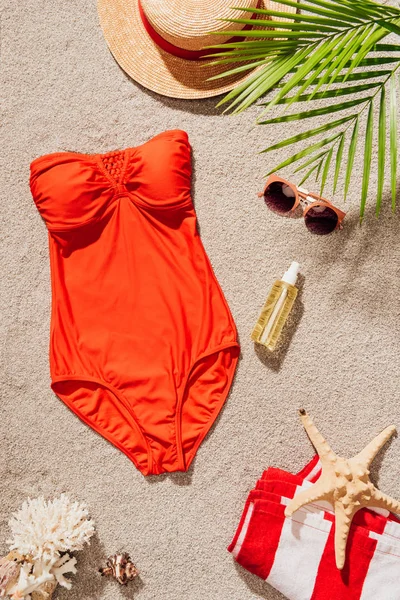 Top view of stylish red swimsuit with accessories lying on sandy beach — Stock Photo