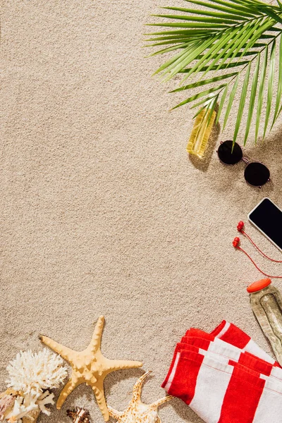 Вид сверху на полосатое полотенце с различными предметами, лежащими на песчаном пляже — стоковое фото