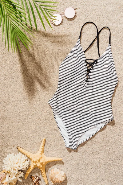 Vue de dessus du maillot de bain élégant avec des lunettes de soleil couché sur la plage de sable — Photo de stock