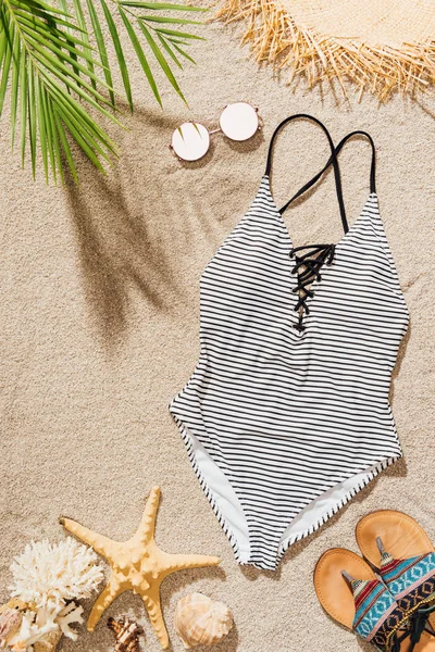 Top view of stylish swimsuit with sunglasses and flip flops lying on sandy beach — Stock Photo