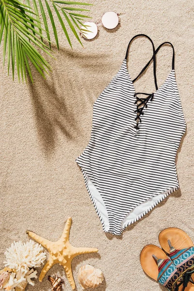 Vista superior del traje de baño con gafas de sol y chanclas tumbadas en la playa de arena - foto de stock