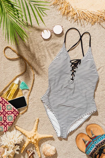 Top view of swimsuit and various female accessories lying on sandy beach — Stock Photo