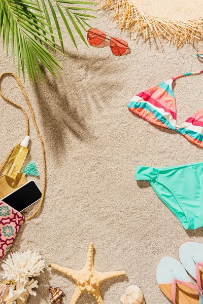 Vista superior del bikini y accesorios que se encuentran en la playa de arena - foto de stock