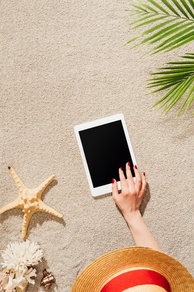 Cropped shot of woman in hat using tablet while relaxing on sandy beach — Stock Photo