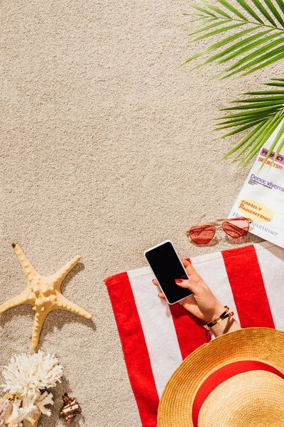 Recortado tiro de la mujer usando el teléfono inteligente mientras se relaja en la playa de arena - foto de stock
