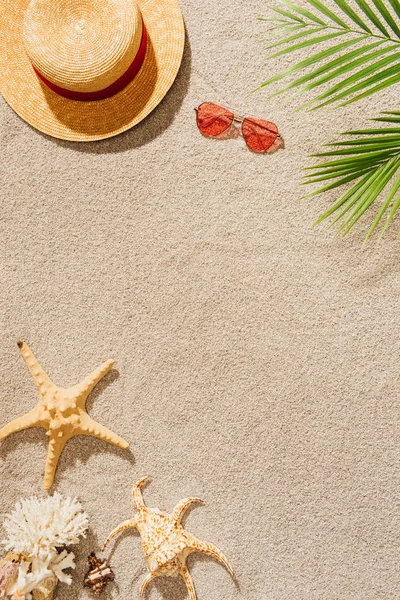 Вид зверху на солом'яний капелюх з сонцезахисними окулярами на піщаному пляжі — стокове фото