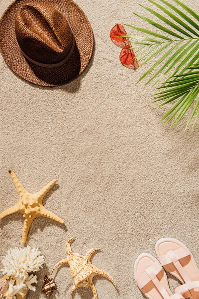 Vue de dessus du chapeau de paille élégant avec des lunettes de soleil et des sandales sur la plage de sable — Photo de stock