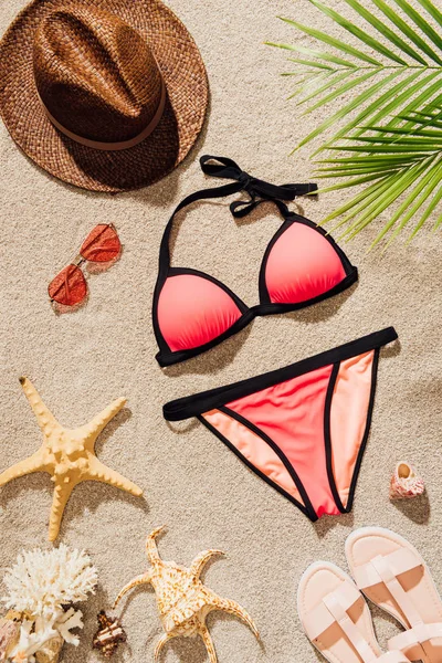 Top view of stylish bikini lying on sandy beach with accessories — Stock Photo