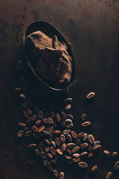 Vista superior de deliciosas piezas de chocolate y granos de cacao en la superficie oscura - foto de stock