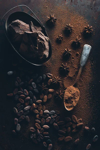 Vue de dessus de délicieux morceaux de chocolat, fèves de cacao et cuillère avec de la poudre de cacao sur la surface sombre — Photo de stock