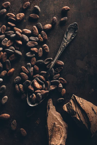 Top view of cocoa beans, vintage spoon and chocolate pieces on dark surface — Stock Photo