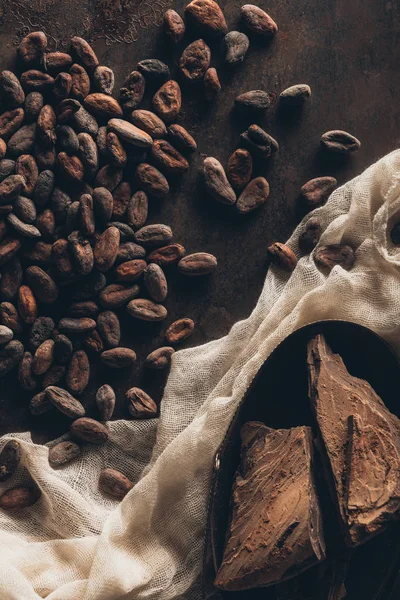 Верхний вид вкусных кусочков шоколада, ткани и какао-бобов на темной поверхности — стоковое фото