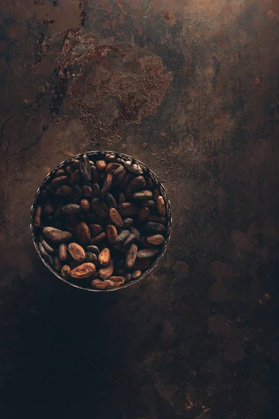 Vista dall'alto di deliziosi fagioli di cacao in ciotola vintage su una superficie rustica scura — Foto stock