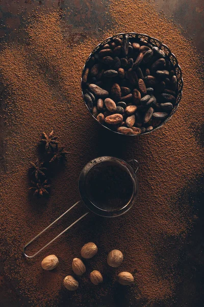 Top view of gourmet cocoa beans in vintage bowl, sieve and star anise on cocoa powder — Stock Photo