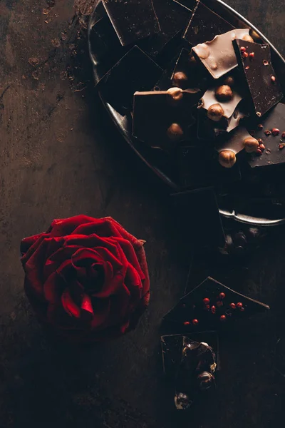 Vista superior de hermosa flor de rosa roja y una variedad de deliciosas piezas de chocolate en la superficie oscura - foto de stock