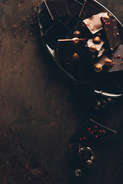 Вид сверху на различные вкусные кусочки шоколада с орехами на темной поверхности — стоковое фото