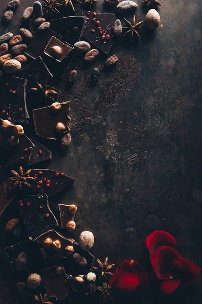 Вид сверху на вкусный шоколад с орехами, анисом и лепестками роз на темной поверхности — стоковое фото
