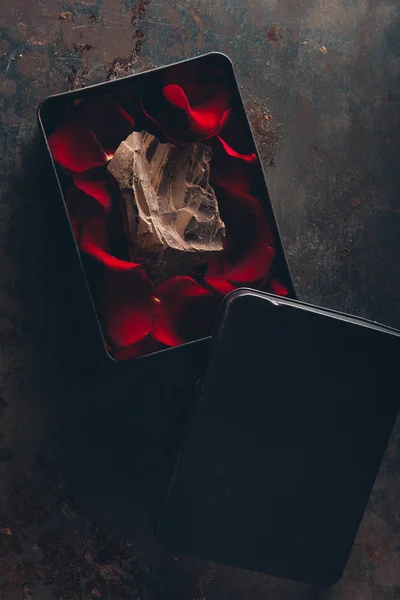 Vue du haut de la boîte avec des pétales de rose rouge et un morceau de chocolat gastronomique — Photo de stock