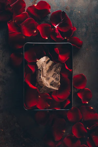 Vue du haut de la boîte avec des pétales de rose rouge et délicieux morceau de chocolat — Photo de stock