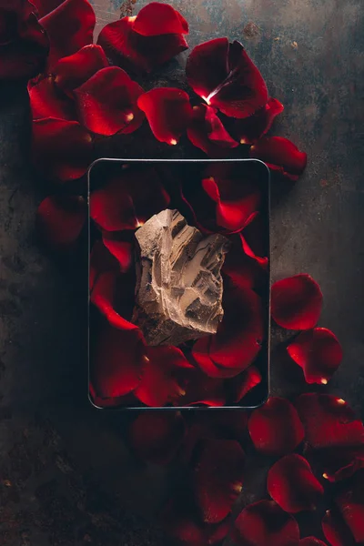 Vista superior de la caja con pétalos de rosa roja y delicioso pedazo de chocolate - foto de stock