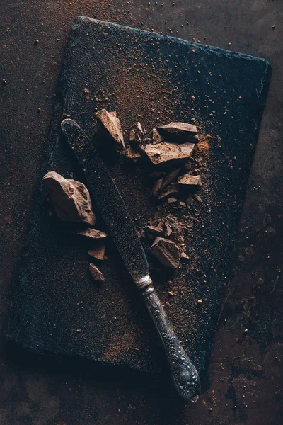 Vista dall'alto di coltelli vintage, pezzi di cioccolato e cacao in polvere su lavagna — Foto stock