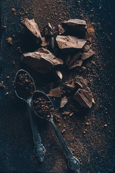 Vista superior de colheres vintage, pedaços de chocolate e cacau em pó na superfície escura — Fotografia de Stock