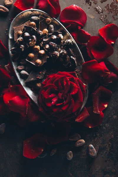 Top view of beautiful red rose petals and gourmet chocolate with hazelnuts on dark surface — Stock Photo