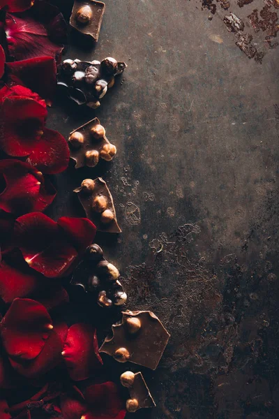 Top view of delicious chocolate pieces with hazelnuts and red rose petals on dark surface — Stock Photo