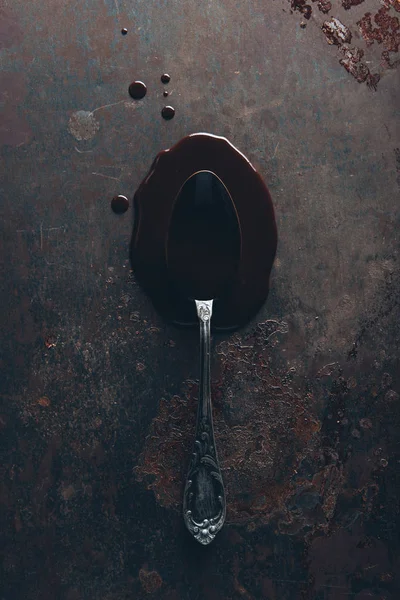 Вид сверху на винтажную ложку и изысканный расплавленный шоколад на темной поверхности — стоковое фото