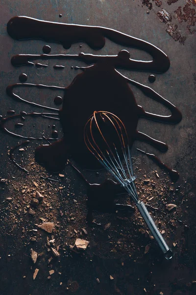 Вид сверху на венчик и вкусный расплавленный шоколад на темной поверхности — стоковое фото