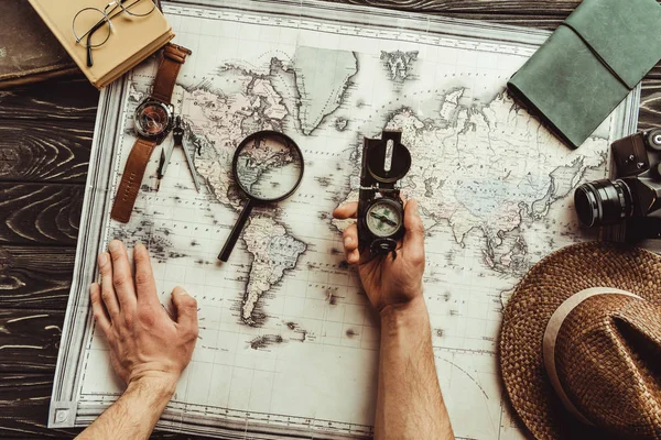 Partial view of man with compass at tabletop with map, magnifying glass, photo camera and hat — Stock Photo