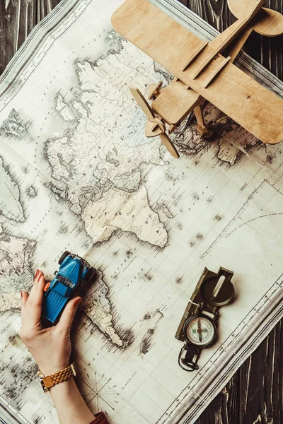 Vista parcial de la mano femenina con coche de juguete, brújula, avión de juguete de madera y mapa en la superficie de madera - foto de stock