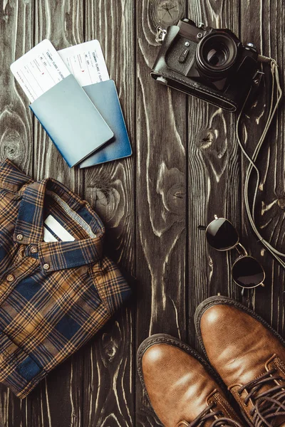 Flat lay with shirt, shoes, passports with tickets, sunglasses and retro photo camera on dark wooden surface — Stock Photo