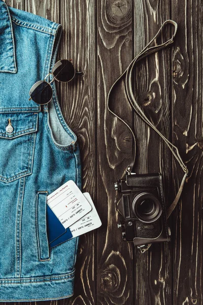 Pose plate avec gilet en denim, passeports, billets, lunettes de soleil et appareil photo rétro sur une surface en bois sombre — Photo de stock
