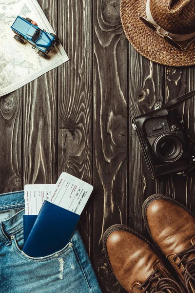 Cama plana con pantalones de mezclilla, zapatos, sombrero de paja, cámara de fotos retro, pasaportes con entradas en la mesa de madera oscura - foto de stock