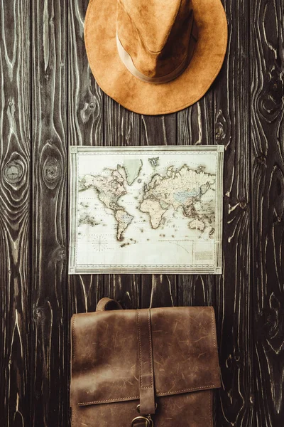 Vista superior del sombrero arreglado, mapa y bolso en la superficie de madera oscura - foto de stock