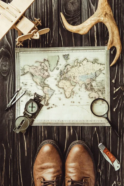 Vue de dessus du cadre de voyage avec carte, chaussures, boussole, loupe et cornes décoratives sur une surface en bois sombre — Photo de stock