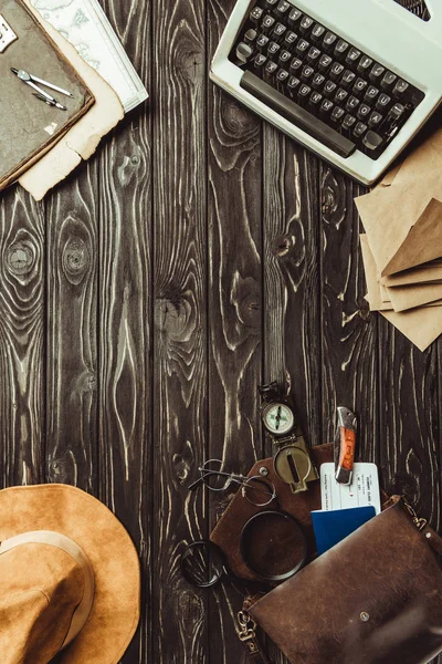 Cama plana con máquina de escribir, sobres, sombrero, bolsa con lupas, pasaporte, billete y navaja en la superficie de madera oscura - foto de stock