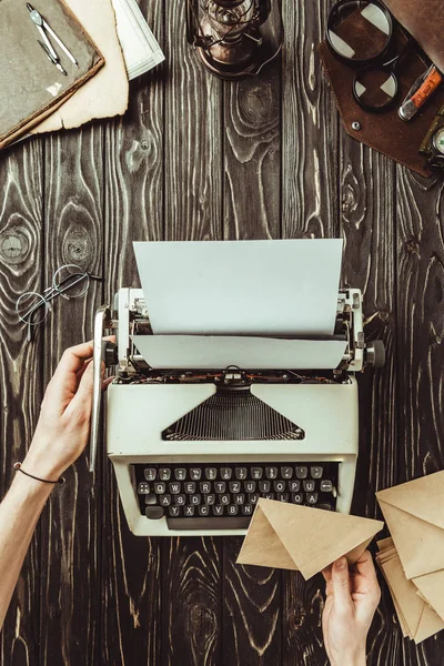 Partial view of female hands, typing machine, magnifying glasses and envelopes on wooden tabletop — Stock Photo