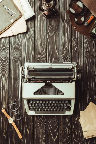 Tendido plano con máquina de escribir, sobres, anteojos, bolsa con lupas y navaja en la superficie de madera oscura - foto de stock
