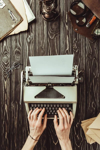 Teilansicht des Schreibens auf Schreibmaschine mit leeren Umschlägen und Lupe auf Holztischplatte — Stockfoto
