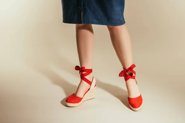 Imagen recortada de mujer con estilo en sandalias de plataforma roja sobre fondo beige - foto de stock