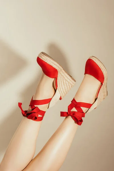 Imagen recortada de patas femeninas al revés en elegantes sandalias de plataforma roja sobre fondo beige - foto de stock