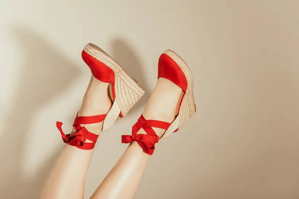 Tiro recortado de patas femeninas al revés en sandalias de plataforma roja sobre fondo beige - foto de stock