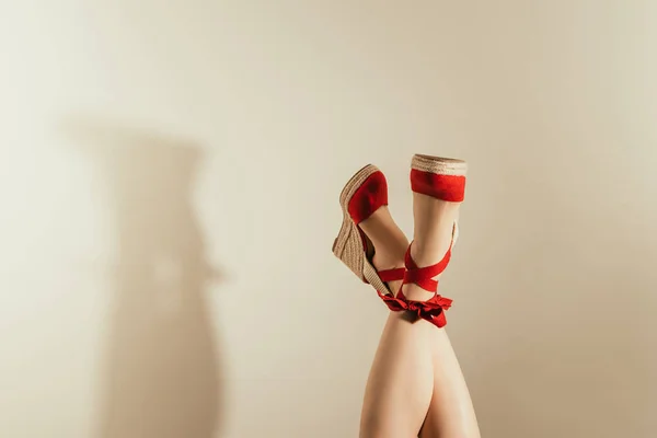 Tiro recortado de patas femeninas boca abajo en sandalias de plataforma roja sobre fondo beige - foto de stock