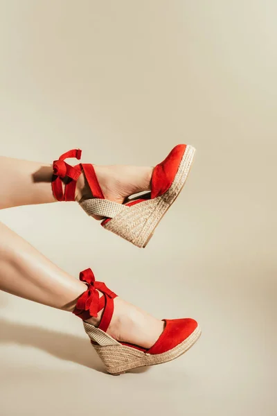 Tiro recortado de piernas de mujer en elegantes sandalias de plataforma roja sobre fondo beige - foto de stock