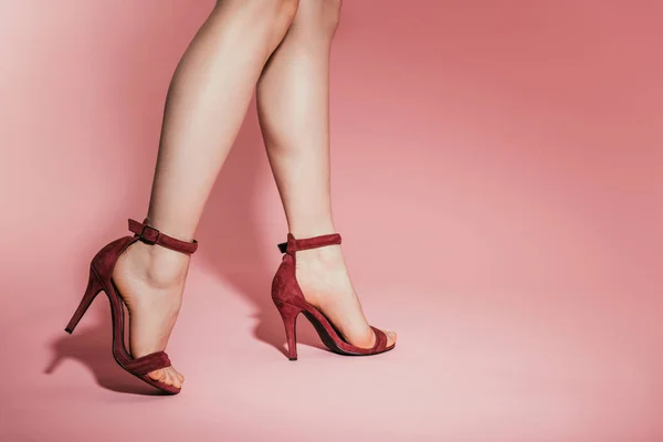 Imagen recortada de piernas de mujer en sandalias de tacón alto con estilo sobre fondo rosa - foto de stock