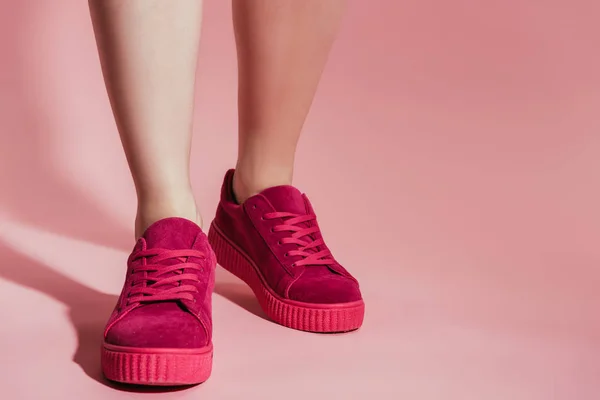 Immagine ritagliata di gambe di donna in scarpe da ginnastica alla moda su sfondo rosa — Foto stock